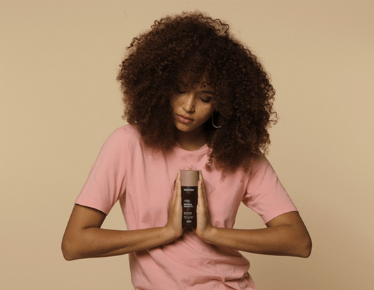 Girl with curly, brown hair holds the Restora Shampoo between her hands.